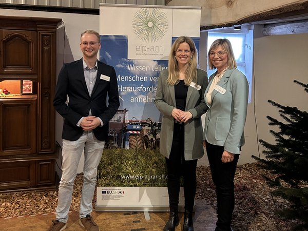 Drei Menschen stehen vor einem Rollup mit dem Logo von EIP